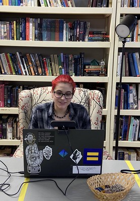 A student in our theater class, using their laptop computer while working on a screenplay, sits in front of a bookshelf.