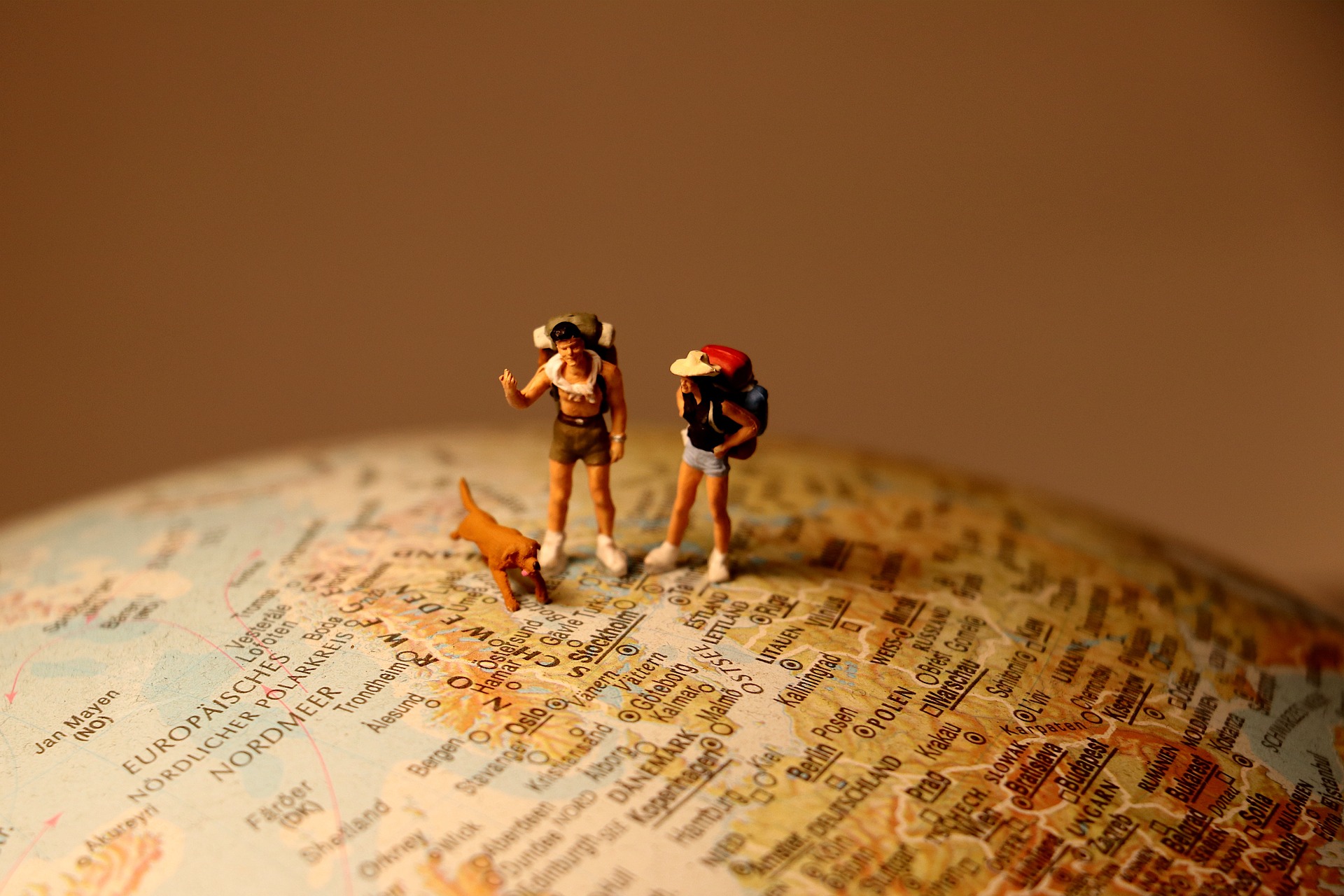 Miniature backpackers and pup stand on a globe.