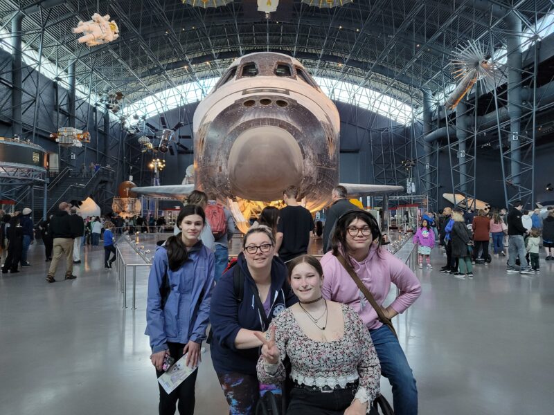 Three students and a teacher stand in front of the Space Shuttle Discovery at Udvar-Hazy