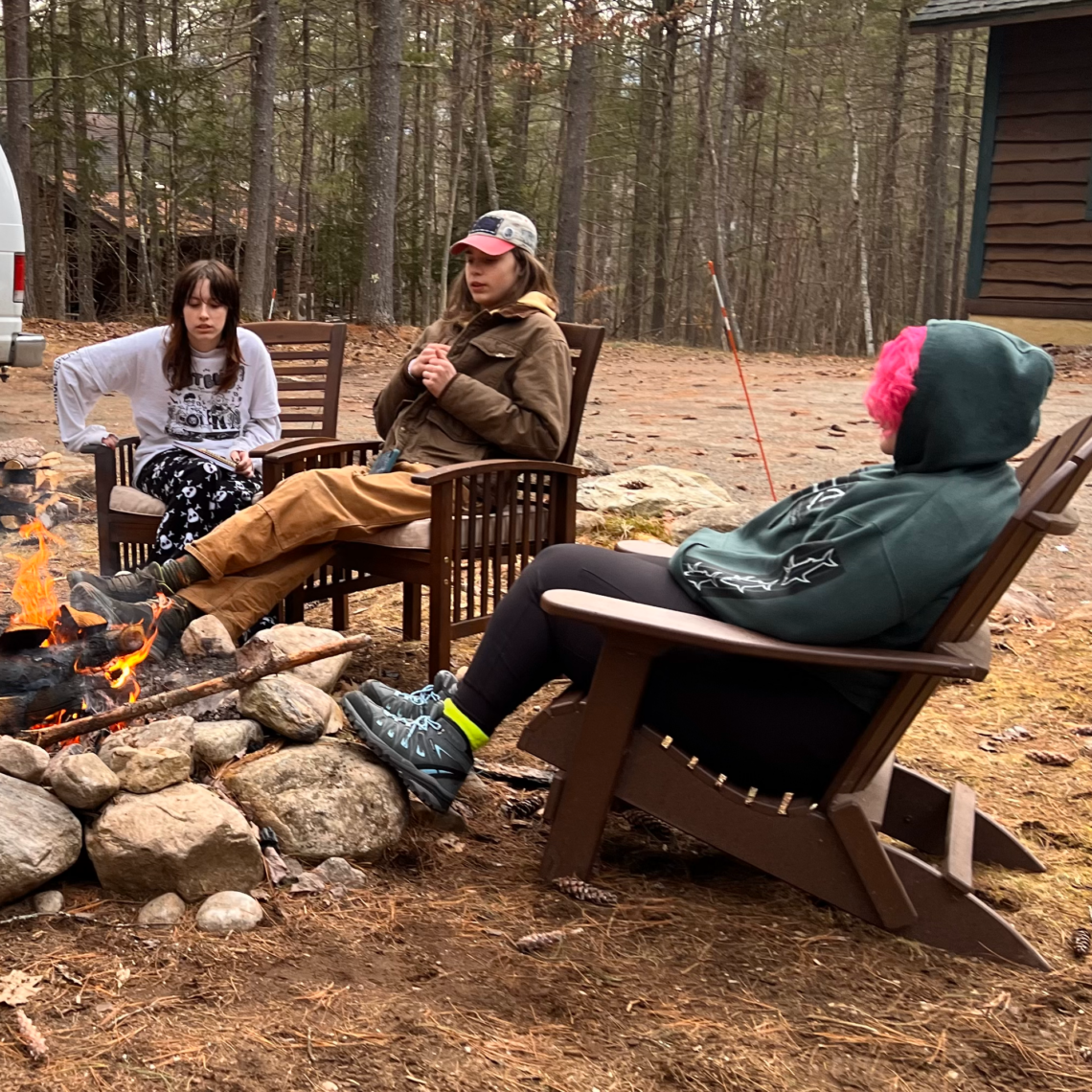Two students and a teacher relax by the campfire