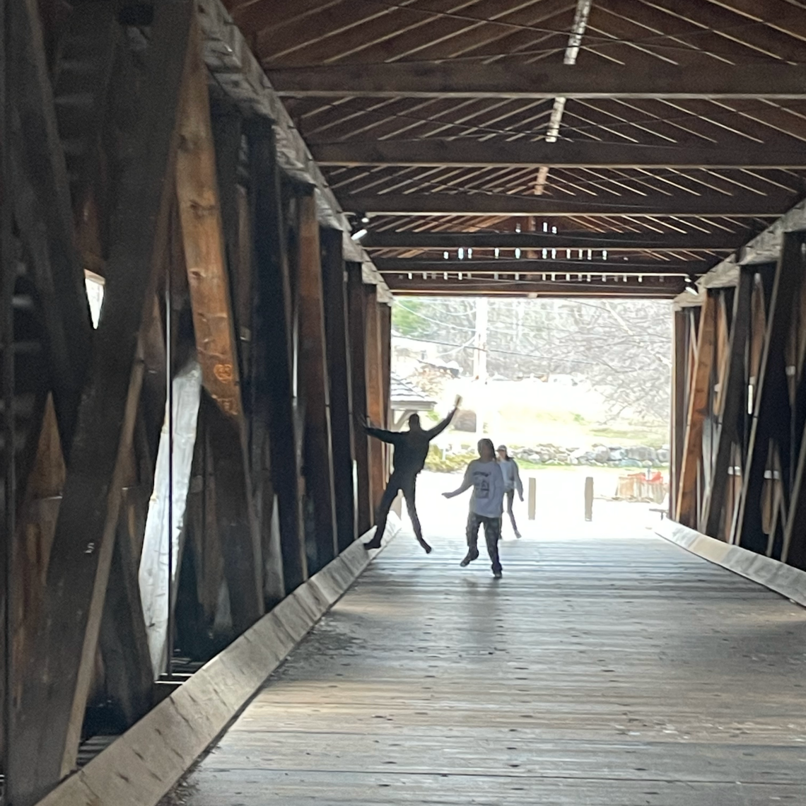 Two students are silhouetted inside a covered bridge.