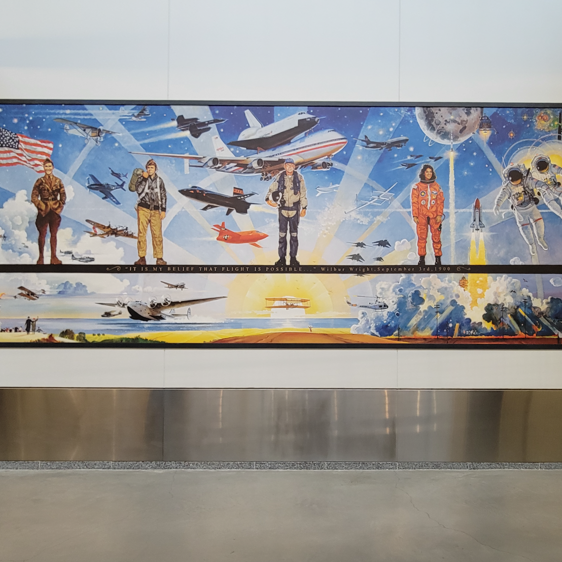 A section of a painting depicting aviators and astronauts with various flying machines behind them with earlier aviation/aviators to the left and more modern ones to the right. A quote from Wilbur Wright reading "It is my belief that flight is possible." is on a dark stripe, upon which aviators stand.