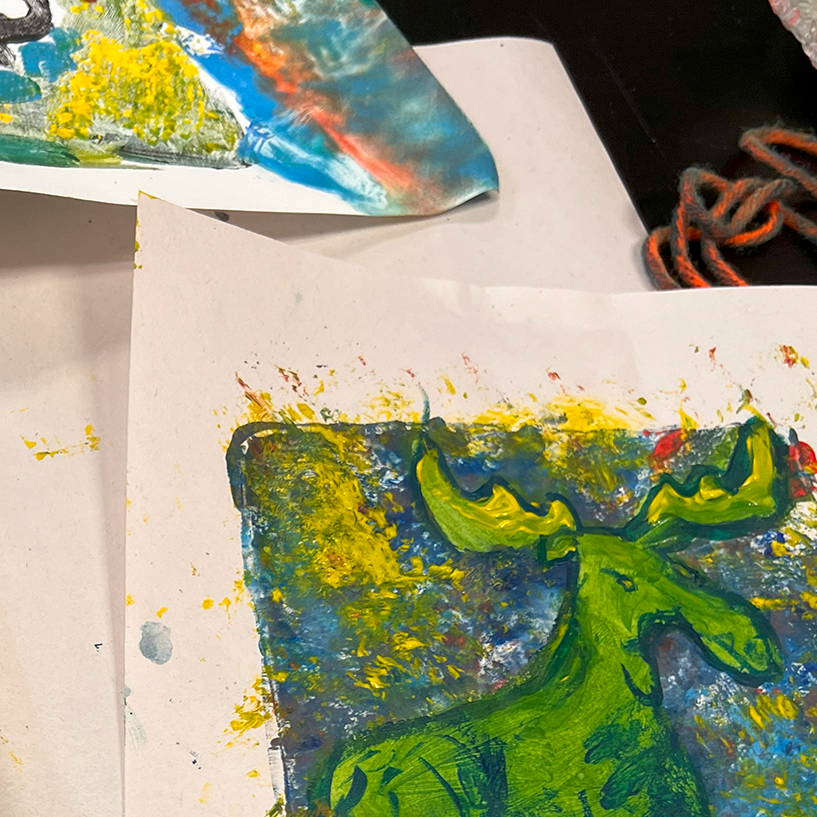 Colorful gel prints, ready for journal cover assembly. In the foreground is a moose in greens and yellows in front of a chaotic background on cream paper.